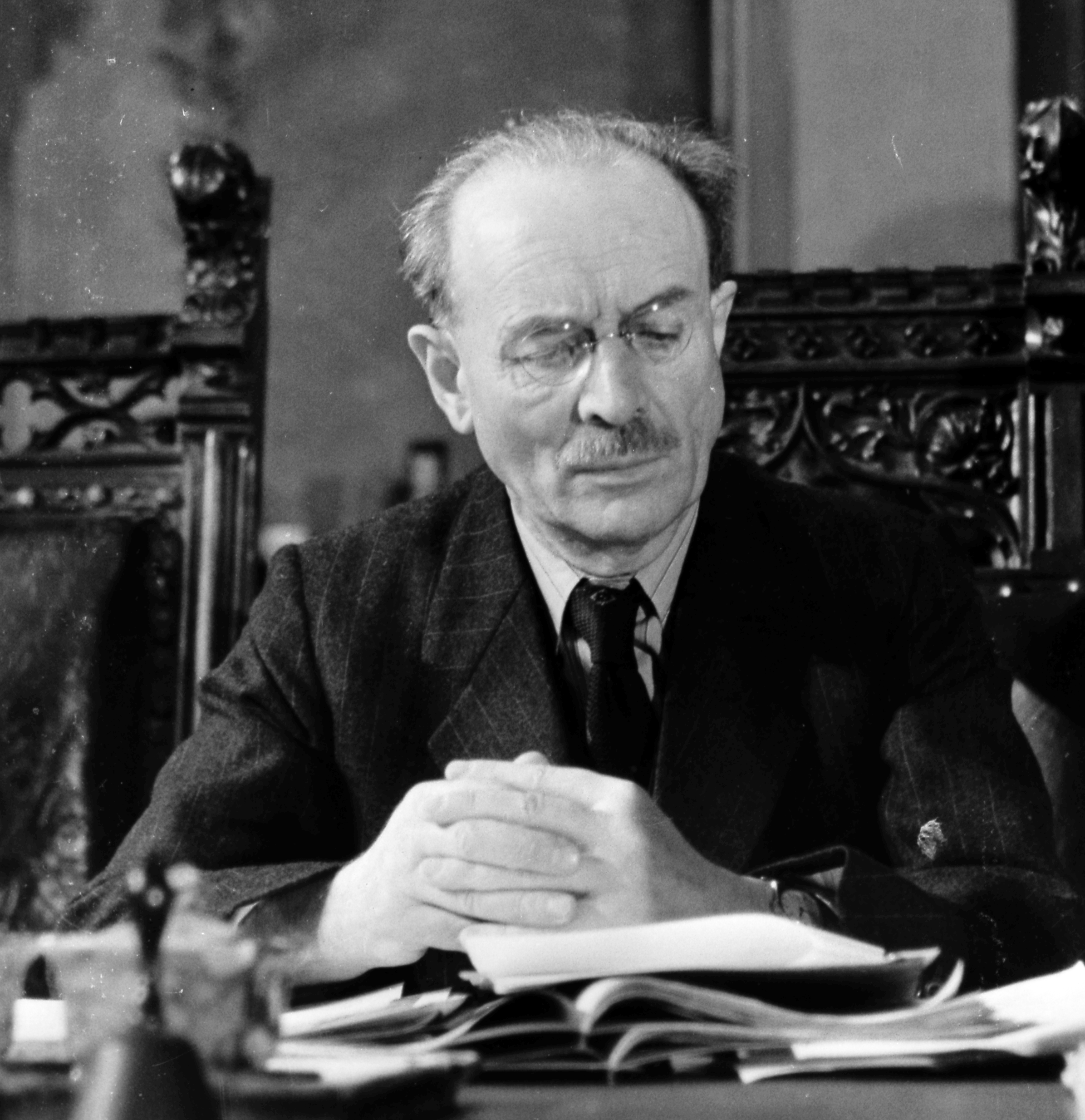 Ministerpräsident Wilhelm Hoegner von der SPD sitzt am Schreibtisch. Er blickt auf die vor ihm liegende Verfassung von 1946